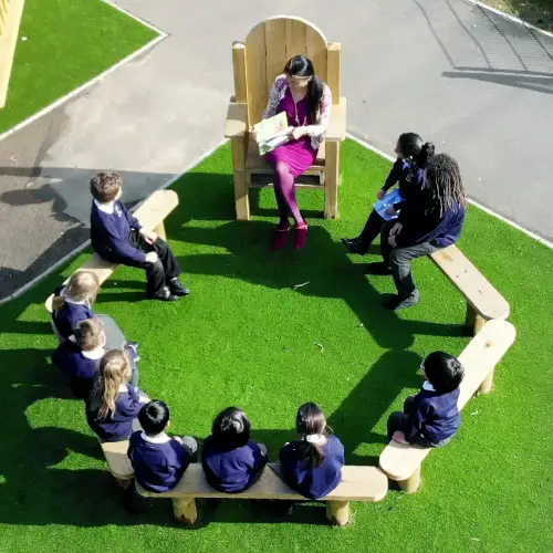 school student sat on school playground benches listening to teacher on storytelling chair