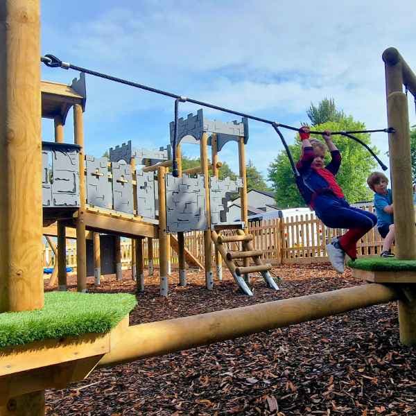 A trim trail with a variety of obstacles and a play castle in the background, as a child completes the trim trail.