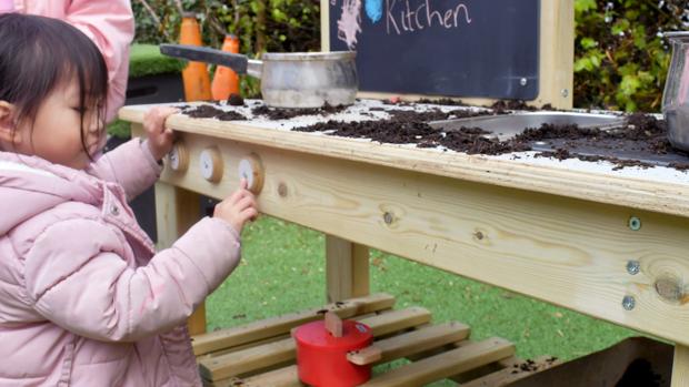 An early years child playing with affordable Mud Kitchen outside