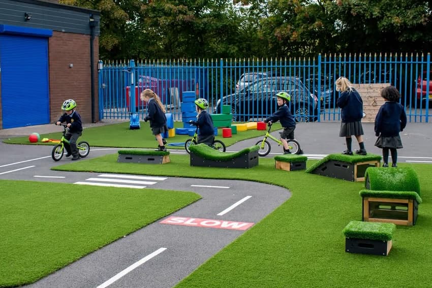 Two nursery children sitting on the floor in a classroom, looking in a mirror on the back of a bookcase.