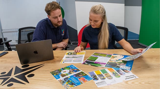 Two members of staff in a meeting room designing a brochure