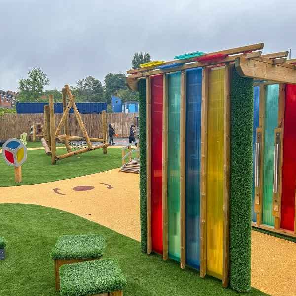 A sensory arbour placed on safety surfacing with freestanding play equipment around.