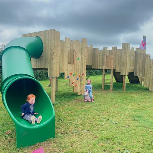 happy child going down large green slide from wooden play castle