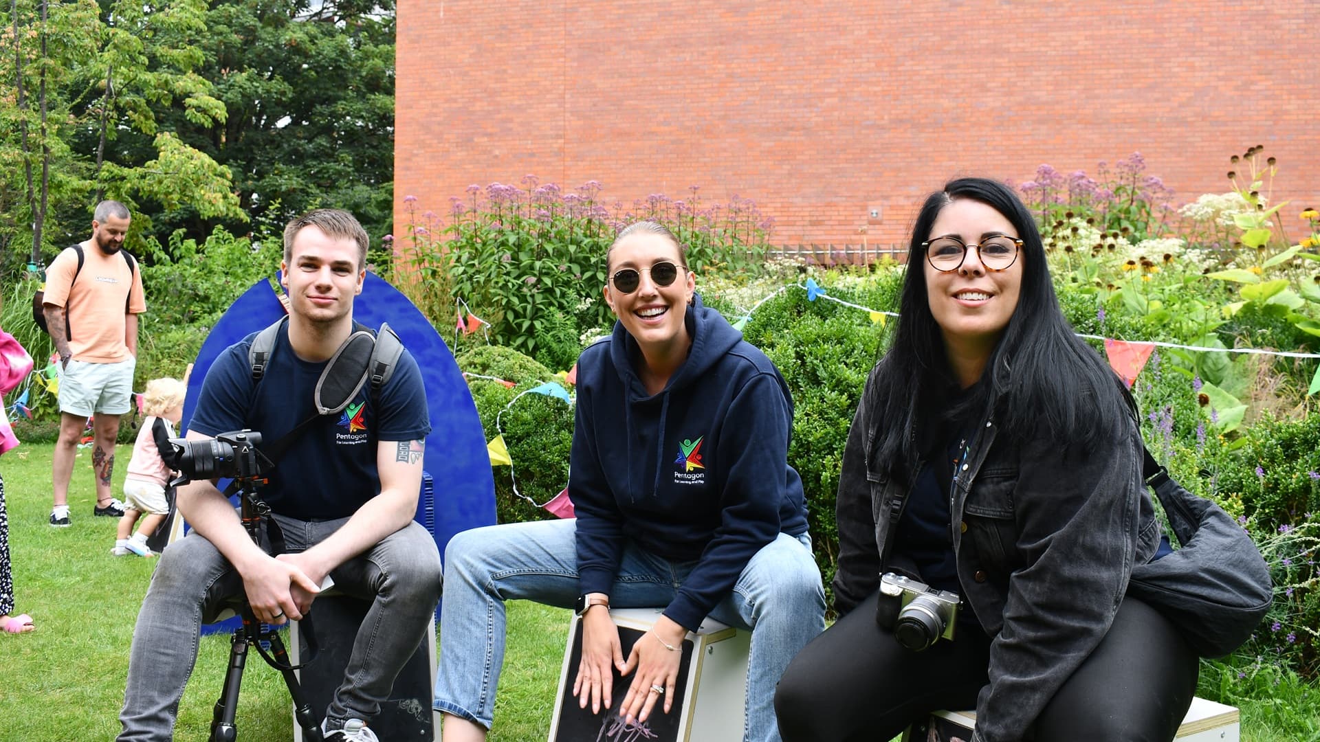 Three team members from Pentagon Play lauging and smiling whilst sat on musicial play equipment