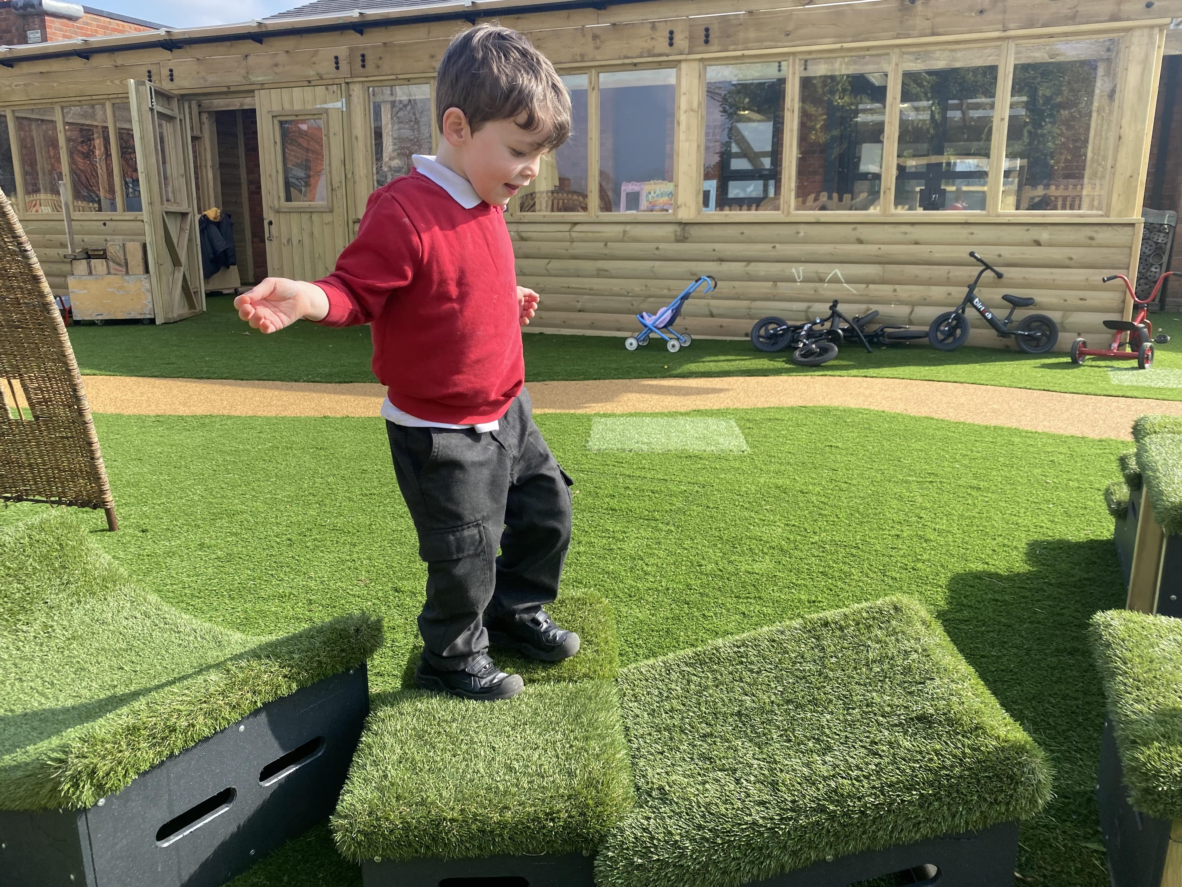 Nursery children playing on grass-topped Get Set, Go! Blocks in the playground.