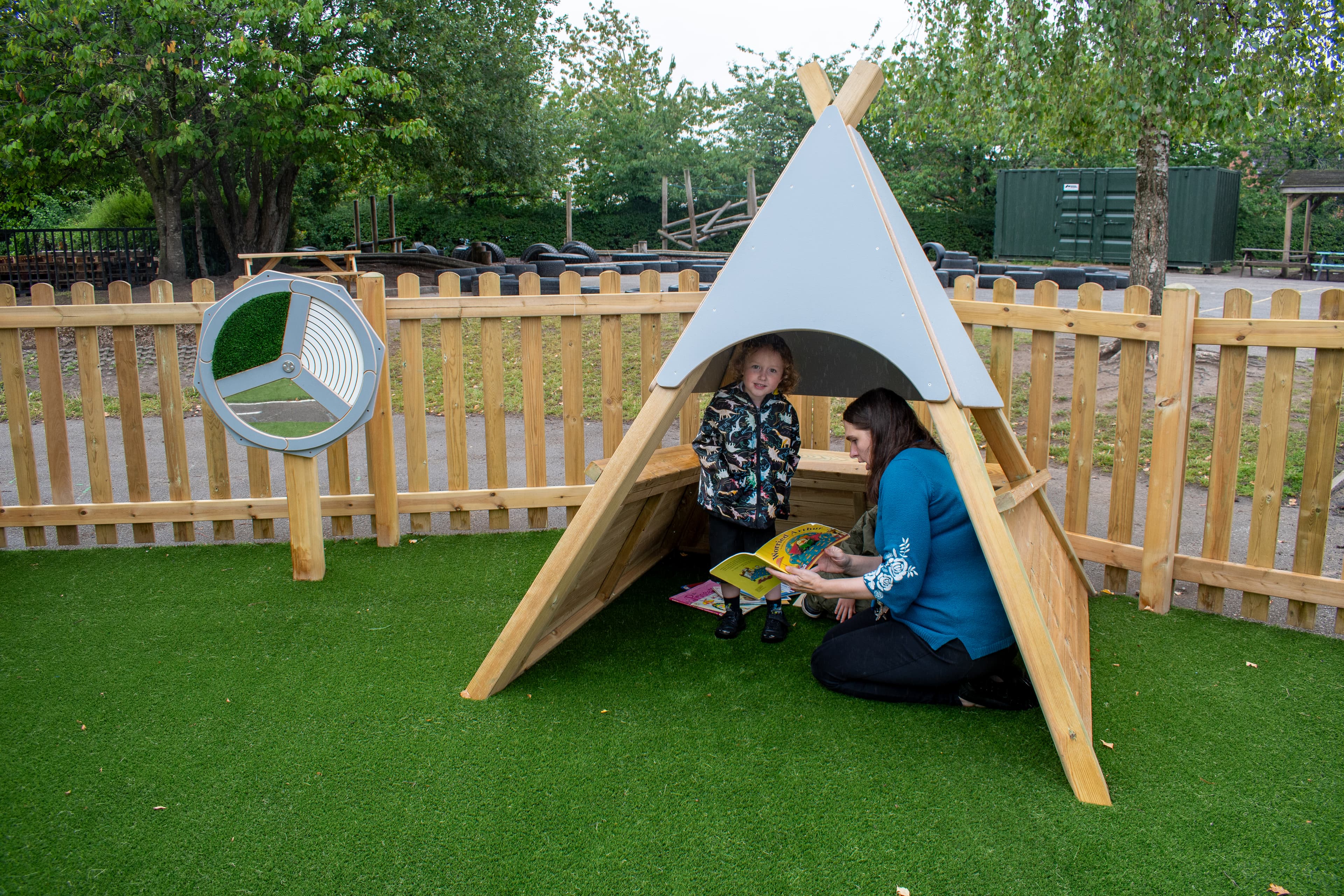 A teacher and a child are reading a book underneath the Wigwam.