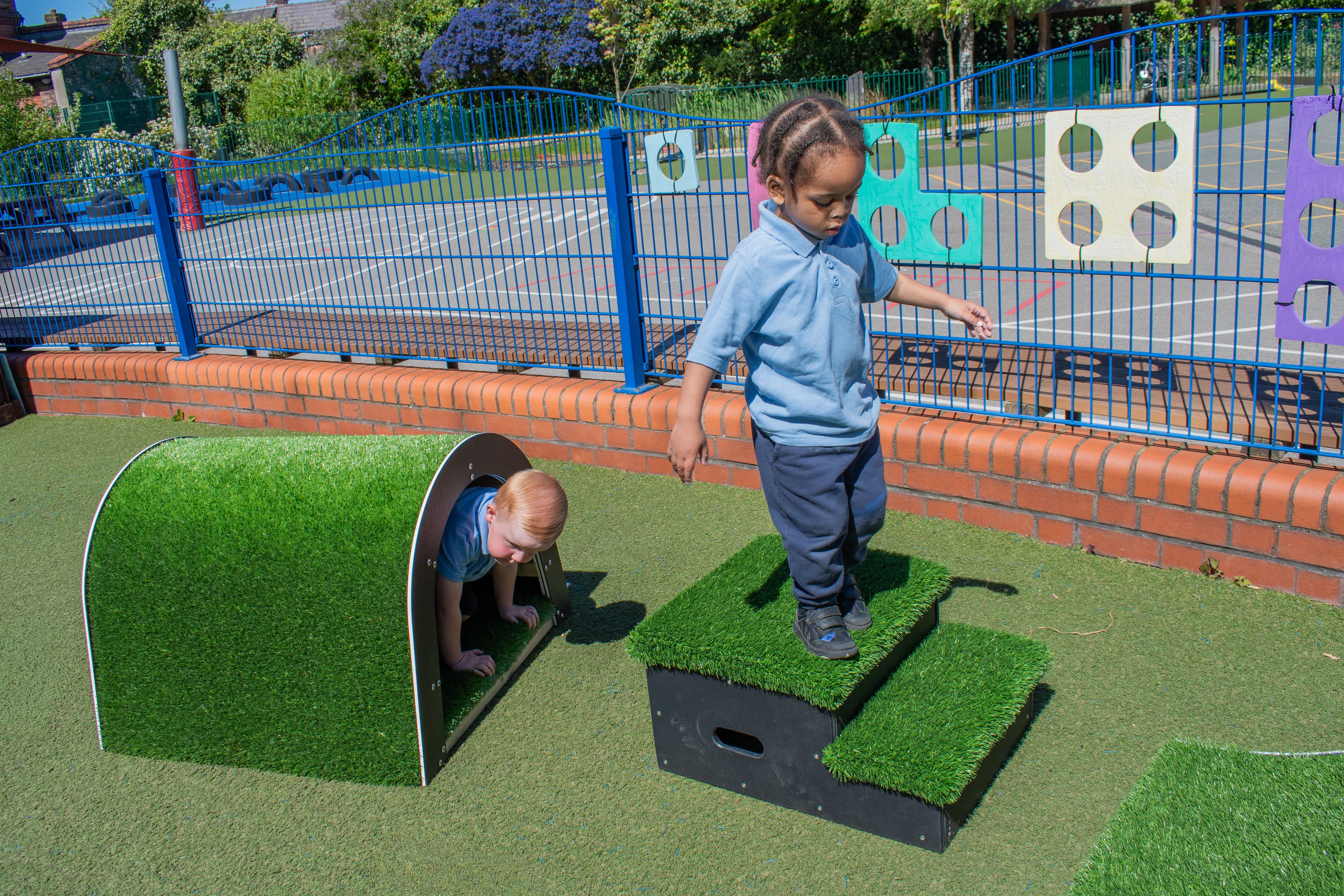 A child is climbing through the tunnel block, as another child is walking down the steps block in front of the tunnel.