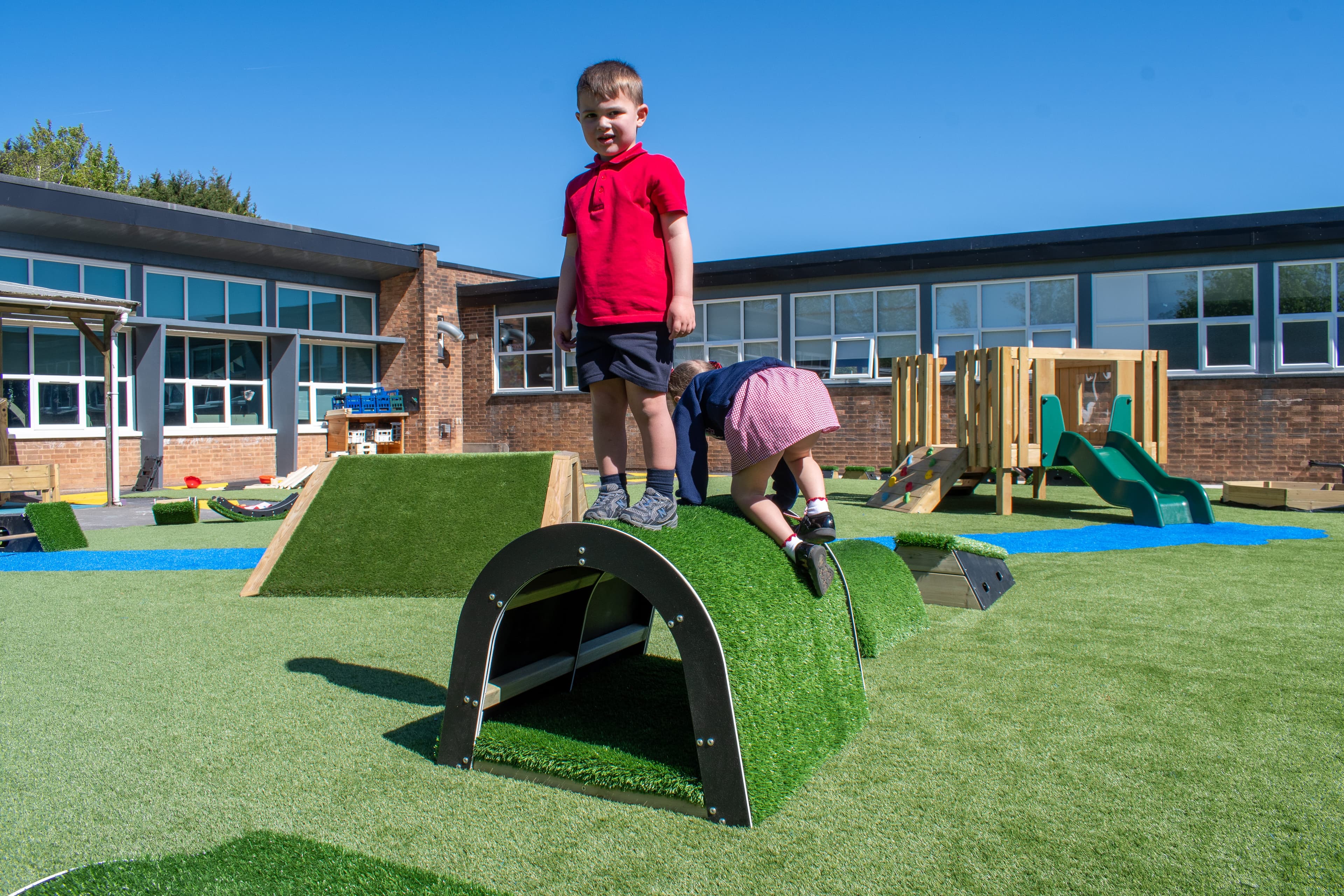 A boy is stood on top of the tunnel block, looking at the camera. A girl is crawling on top of it too, behind the boy.