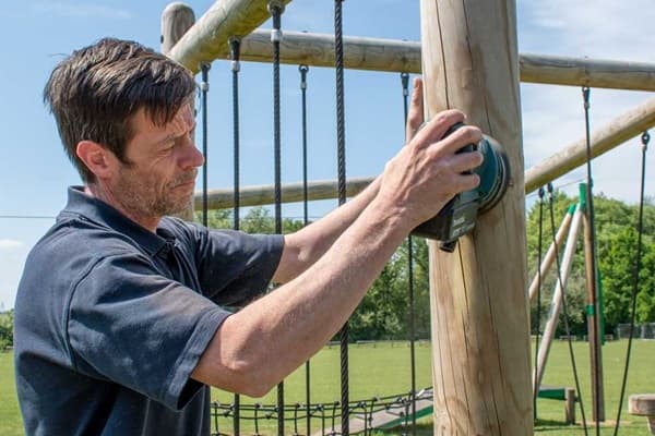 A playground inspector is checking the height of a swing set from the ground to the seat