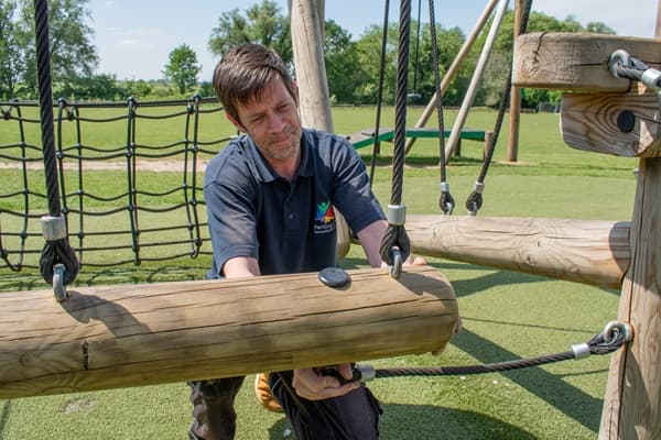 A playground inspector is giving a rope climbing net a pull to ensure that the rope is properly attached to the playground equipment