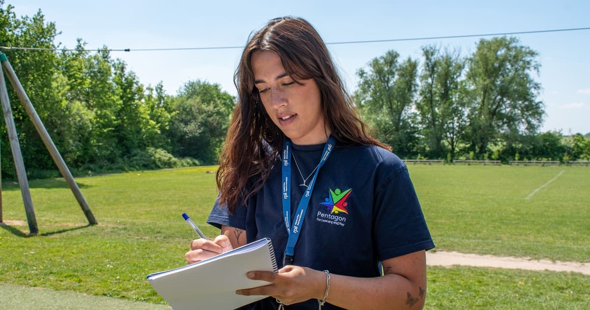 A playground inspector is holding her phone and is dialling a number to call a client, whilst she is stood on the playground