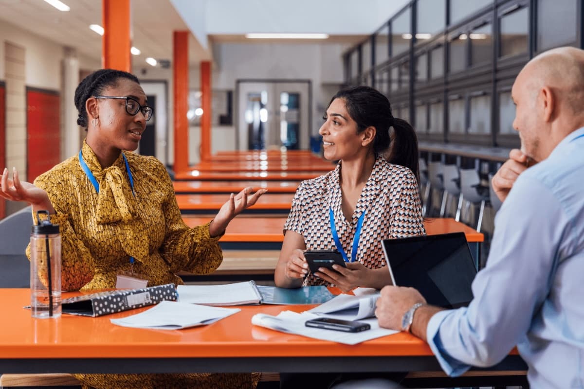 A group of three teachers are sat at a bench and are discussing the school-based nursery scheme with each other.