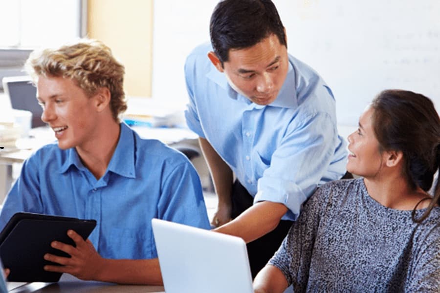 A group of three teachers are sat at a bench and are discussing the school-based nursery scheme with each other.